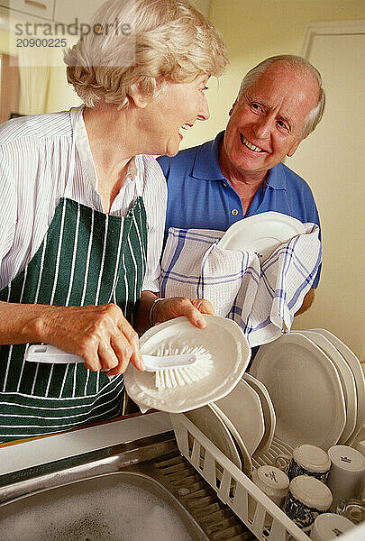 Senior couple washing dishes in the kitchen at home.