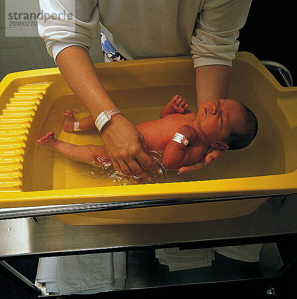 Hospital Maternity Unit. Nurse washing baby. Post-natal care of new-born baby.