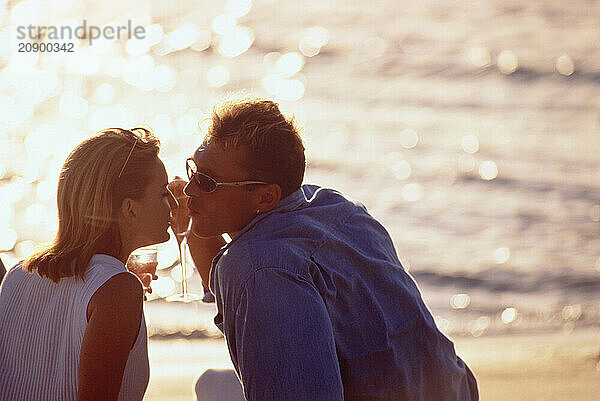 Young man and woman sitting on a beach at sunset.