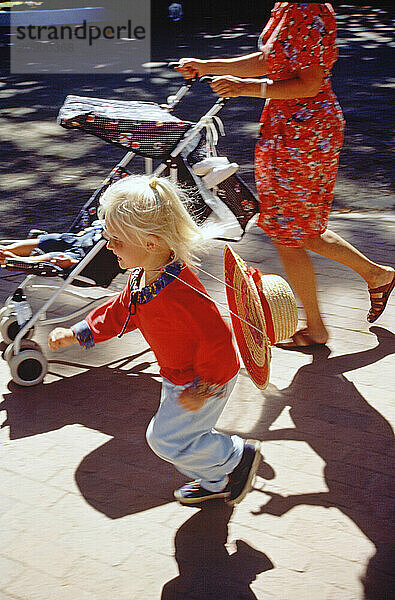 Close up of mother and little girl child pushing pram along city pavement.