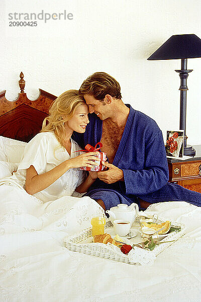 Young couple in bed with special occasion gift and breakfast tray.