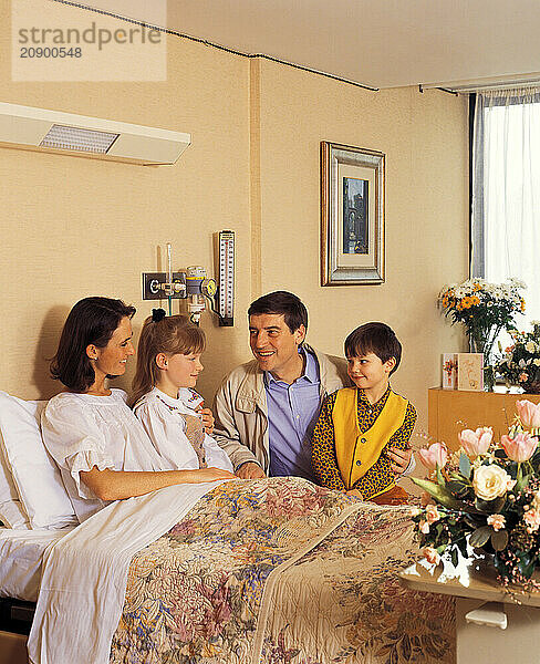 Hospital visit. Man & children visiting woman patient in bed.