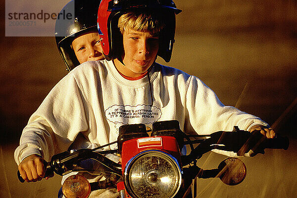 Two teenage boys riding motorcycle.