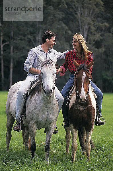 Young couple outdoors riding horses.