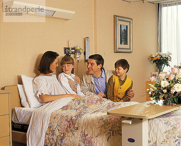 Hospital visit. Man & children visiting woman patient in bed.