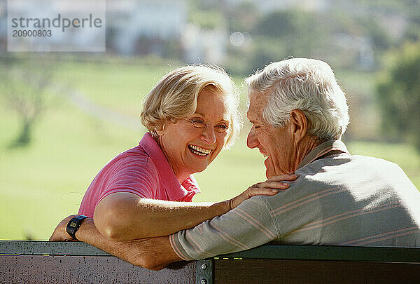 Back view close up of senior man & woman couple sitting outdoors on park bench.