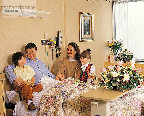 Hospital visit. Woman & children visiting man patient in bed.