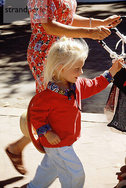 Close up of mother and little girl child pushing pram along city pavement.