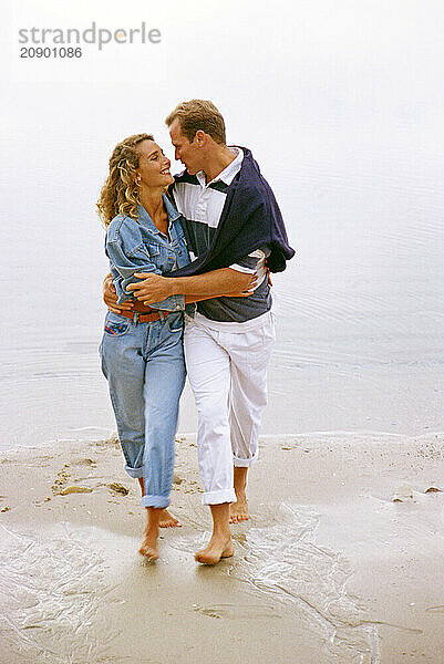 Young couple walking barefoot on the beach.