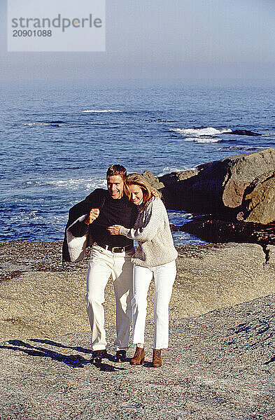 Couple outdoors at the coast walking on rocks.