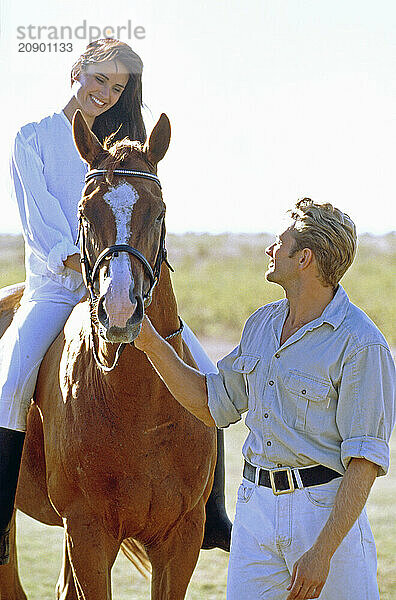 Young couple outdoors with horse. Woman riding bareback.