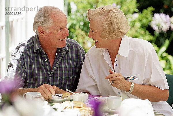 Senior man & woman couple having tea outdoors on garden terrace.