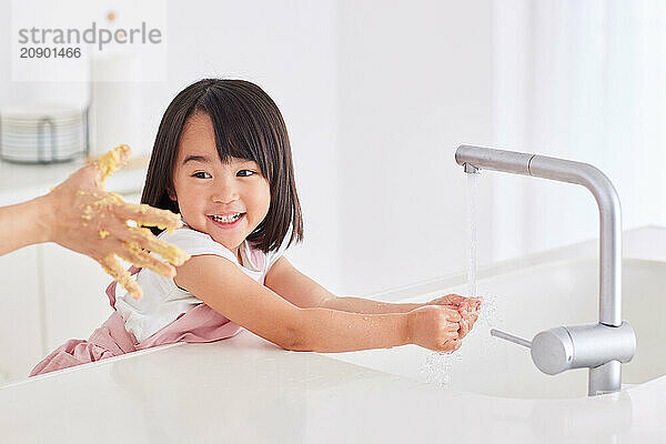 Young Asian girl washing her hands in the kitchen sink