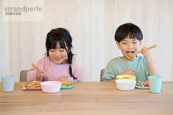 Asian children eating at a table with chopsticks