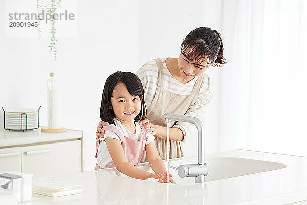 Asian woman and young girl washing their hands in the kitchen sink