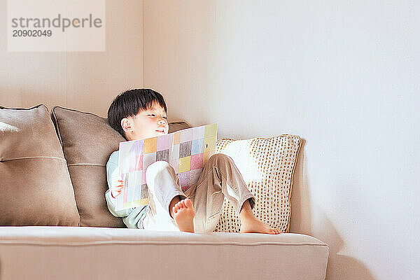 Young Asian boy sitting on a couch reading a book