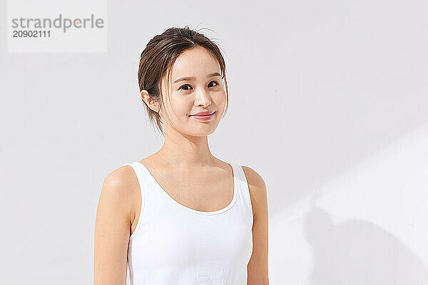 Asian Woman In A White Tank Top Standing In Front Of A White Wall