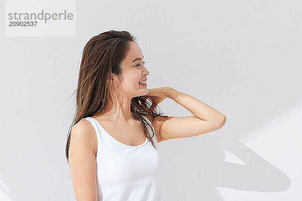 Asian Woman In White Tank Top Standing Against White Wall