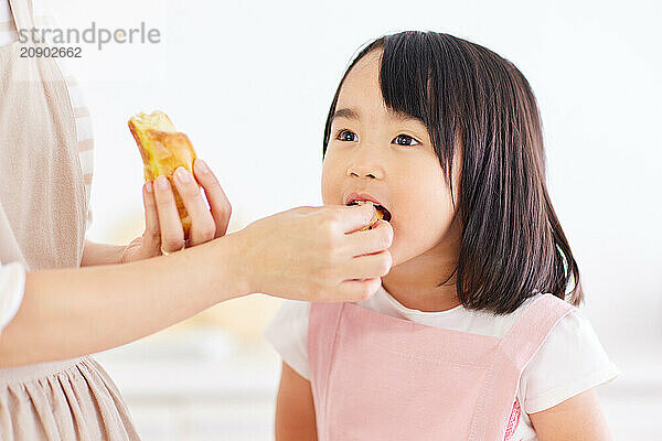 Young Asian girl is eating a piece of bread