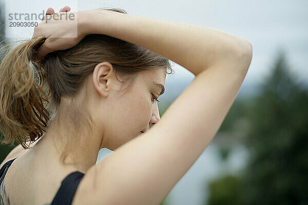 Close-up of a young woman tying her hair in a natural outdoor setting.