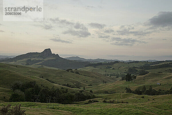 Sunrise over a tranquil  rolling hillside with a distinctive rock formation in the distance under a pastel sky.