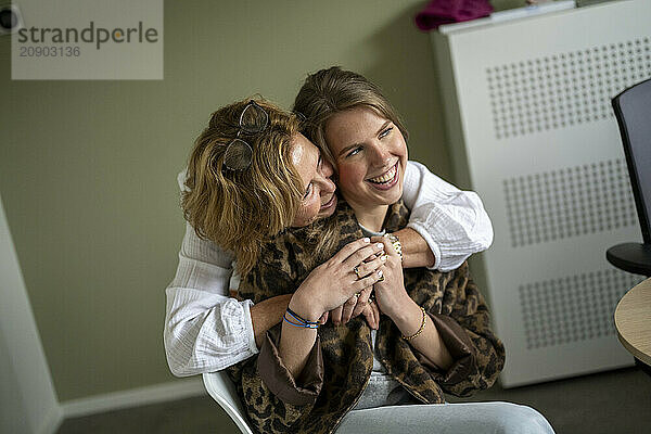 Two women sharing a joyful moment with one embracing the other from behind and both smiling.