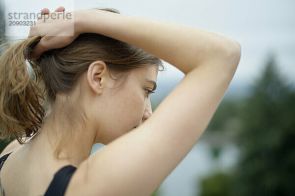 Woman with her hair tied up  viewed from the side against a blurred natural background.