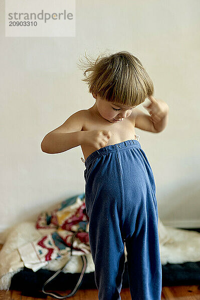 Child trying to dress themselves standing in a room with neutral background.