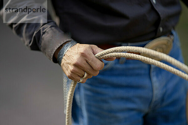 Close-up of a person's hands coiling a rope  dressed in jeans and a dark long-sleeved shirt  with a blurry background.