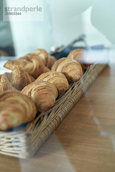 Fresh croissants in a woven basket on a wooden table with a blurred background.