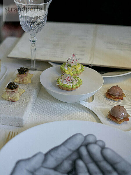 Elegant gourmet appetizers on white porcelain dishes with a backdrop featuring a wine glass  a menu  and a napkin illustrated with a hand sketch.