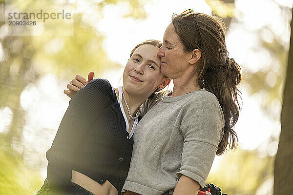 Mother and daughter enjoying a tender moment together outdoors with warm sunlight filtering through the trees.