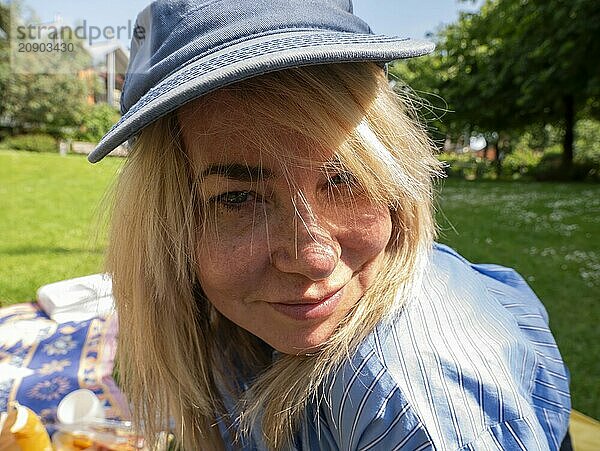 Close-up of a smiling woman wearing a blue hat and striped shirt at a sunny park picnic.