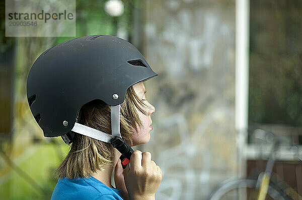 Close-up of a person wearing a black helmet  fastening the chin strap while sitting indoors  with a blurred background.