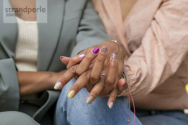 Close-up of two women's hands with colorful nail polish  showcasing friendship and diversity.