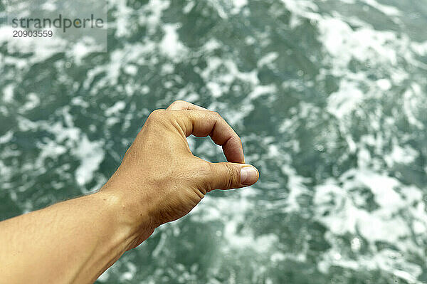 Hand forming an OK gesture against a blurred ocean background