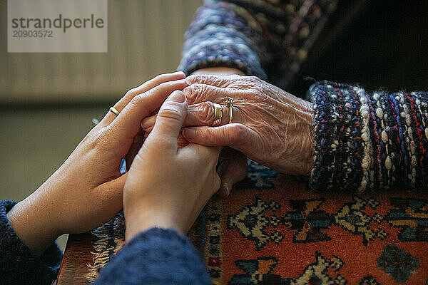 Elderly hands clasped by a younger person's hands on a wooden surface with warm background tones.