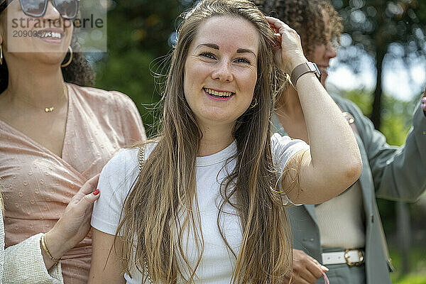 Smiling woman with long hair enjoying a sunny day outdoors with friends in the background.