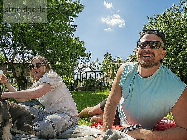 Friends enjoying a sunny picnic with a dog in a lush green park.