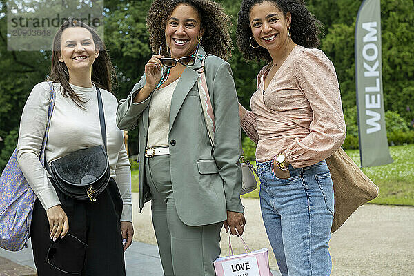 Three women smiling and enjoying a day out  one holding a pair of sunglasses and a shopping bag with the word 'LOVE'.