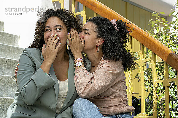 Two women laugh and share a secret on the steps of a cozy home.