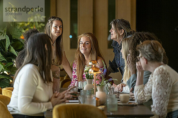 A group of women engaging in lively conversation around a table in a cozy caf? setting.