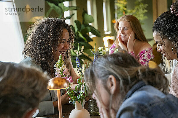 Friends gather around a table in a cozy setting  enjoying each other's company and conversation amidst indoor plants.