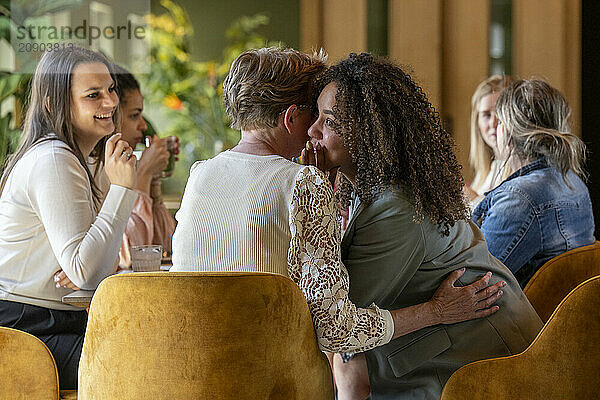 Two couples enjoying time together at a cozy cafe with one couple engaged in conversation while the other shares a romantic kiss.