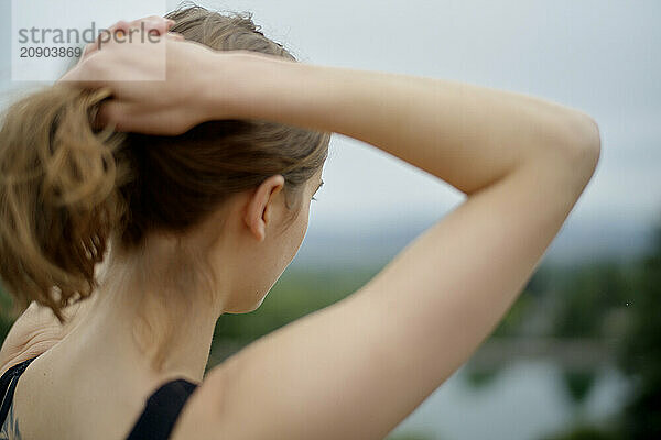 Rear view of a woman tying her hair up with a blurred natural backdrop.