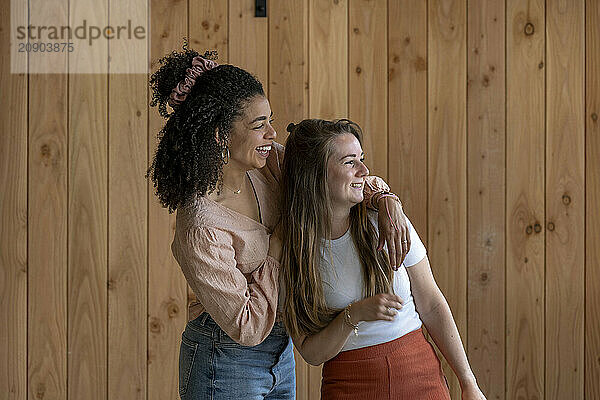 Two happy women embracing and smiling against a wooden wall background.