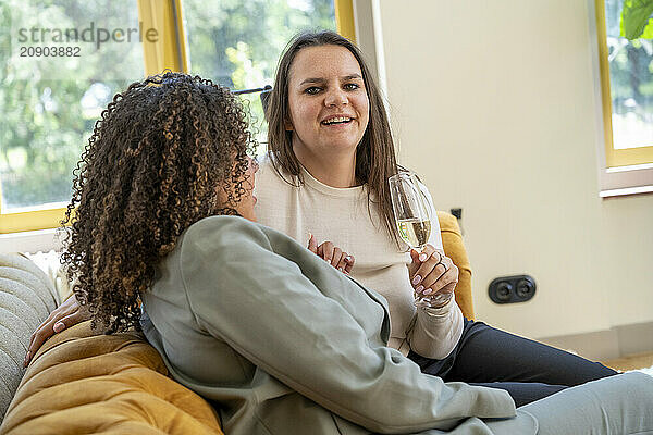 Two women enjoying a conversation on a couch with one holding a glass of white wine.