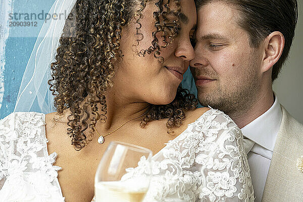 Interracial couple in wedding attire sharing an intimate moment with their foreheads together  smiling with eyes closed.