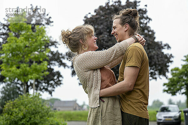 Two women embrace each other warmly in a rural setting  both smiling joyfully.