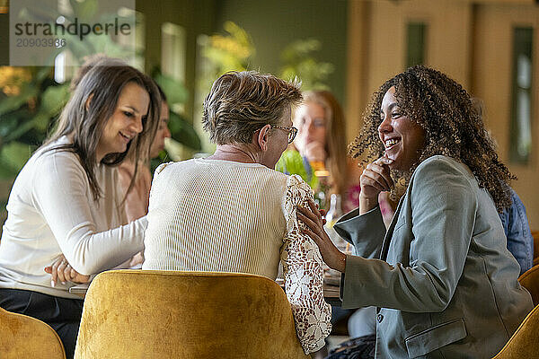 Group of women enjoying a cheerful conversation on yellow velvet chairs with drinks in hand.